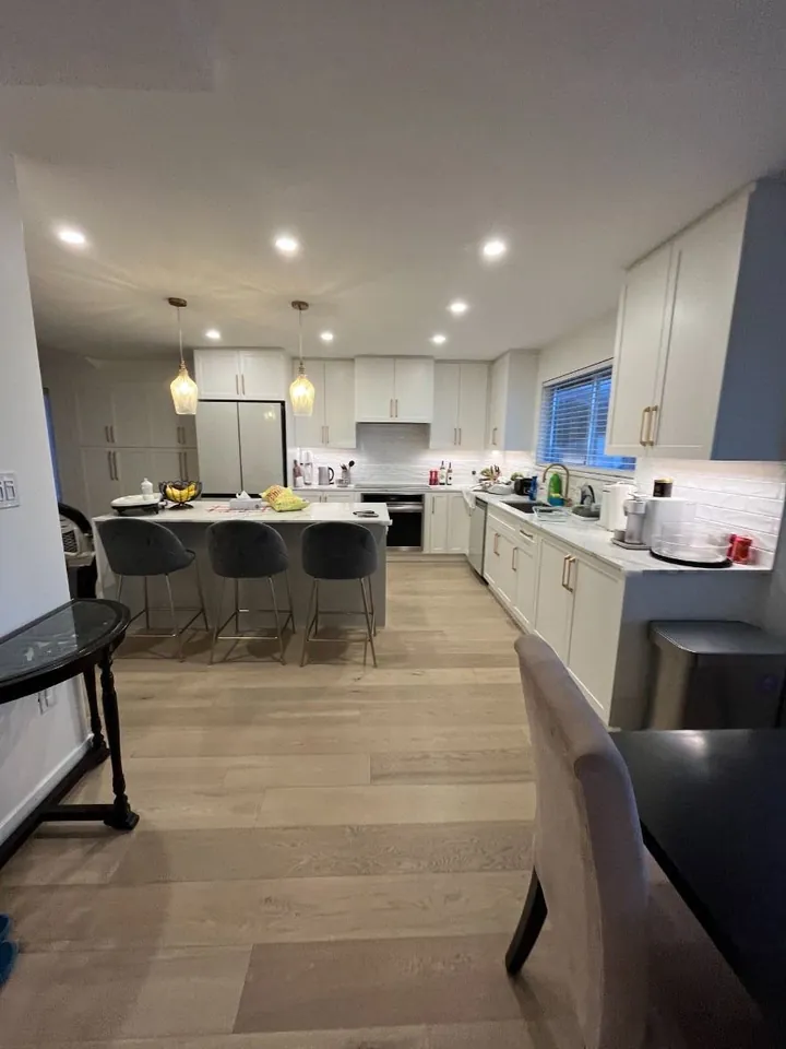 Kitchen with white cabinets, island seating and a dining area on wood flooring