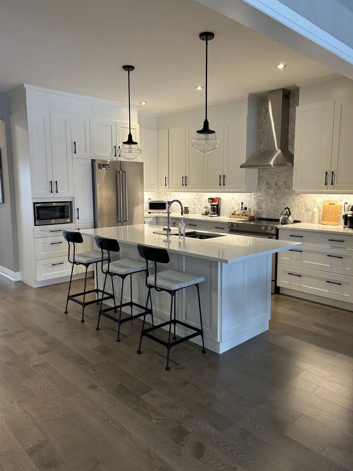 Kitchen with white cabinetry, a quartz island with bar stools and pendant lights
