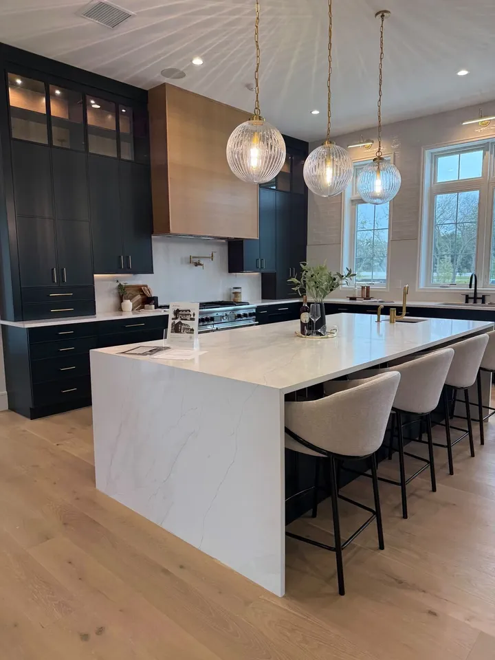 Open kitchen with a white marble island, bar stools, pendant lights and dark cabinetry